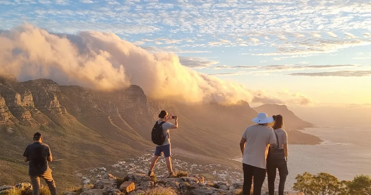 Un piccolo gruppo in cima alla montagna che guarda le nuvole riversarsi oltre il bordo nella luce dorata