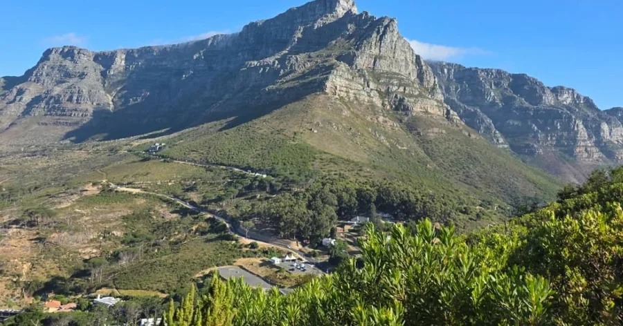 Die Vorderseite des Tafelbergs und seine Grate über grünen unteren Hängen unter blauem Himmel