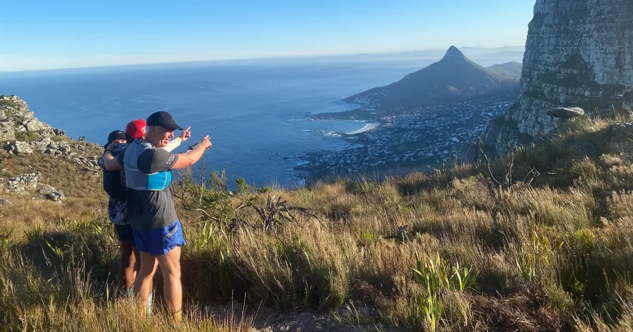 Zwei Wanderer an einem Grashang fotografieren den Lion's Head und den Atlantik
